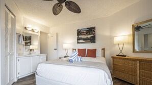 Une chambre à coucher avec un lit, une commode, un miroir, un tableau et un ventilateur de plafond.
