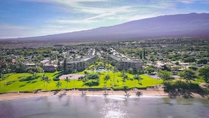 A coastal resort with a central building surrounded by palm trees, a beach, and a mountain in the background. - Oceanview suite nicely renovated B310 at Maui Sunset (Kihei)