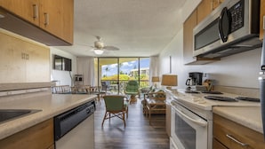 A kitchen with wooden cabinets, a microwave, a dishwasher, and a view of the outdoors. - Oceanview suite nicely renovated B310 at Maui Sunset (Kihei)
