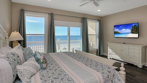 Une chambre avec un grand lit, un téléviseur fixé au mur, un balcon avec vue sur l’océan et une commode blanche.