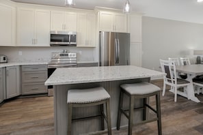 Cozinha moderna com armários brancos, eletrodomésticos de aço inoxidável, bancada de granito e dois banquetas.
