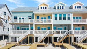 Un immeuble à plusieurs étages situé en bord de mer, doté de balcons, d’une terrasse couverte et d’une plage de sable au premier plan.