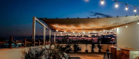 An outdoor patio with a canopy, string lights, lounge chairs, and a bar area.