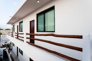 A modern building with white exterior walls, large windows, and a wooden balcony railing.