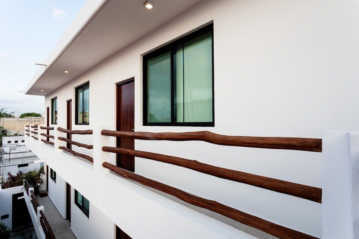 A modern building with white exterior walls, large windows, and a wooden balcony railing.