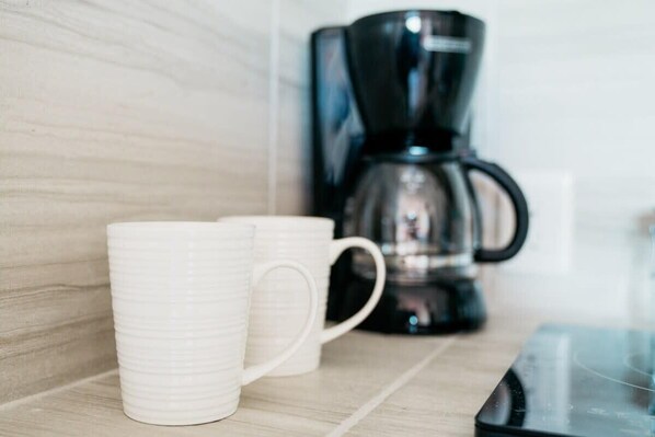 A kitchen counter with two white mugs and a black coffee maker.