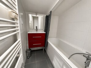 Ein Badezimmer mit einer weißen Badewanne, einem roten Waschtisch mit Schubladen, einem Spiegel über dem Waschbecken und einer Duschvorhang.
