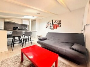 Ein modernes Wohnzimmer mit einem grauen Sofa, einem roten Couchtisch und einer Küche im Hintergrund.