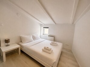 Ein Schlafzimmer mit Bett, Nachttisch, Lampe, Fenster und Heizkörper.