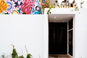 A modern building with a colorful mural on the exterior wall, a black door, and some greenery on the ground.