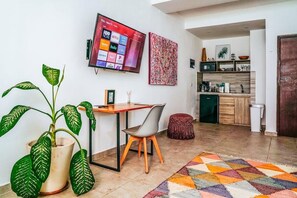 A modern living room with a flat-screen TV, a dining table, a potted plant, and a colorful rug. - King Studio Walk to Beach + Rooftop Pool (Playa del Carmen)