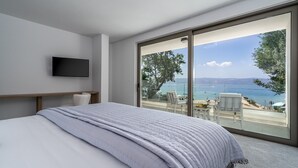 Ein Schlafzimmer mit einem großen Bett, einem Flachbildfernseher und einem Balkon mit Blick auf das Meer und den Strand.