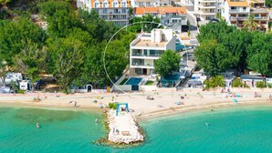 Ein Luftbild einer Küstenregion mit Strand, einem Felsen mit einem Gazebo und einer Reihe von Wohnhäusern mit Balkonen.