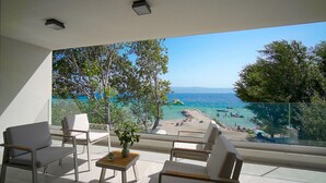 Ein Balkon mit weißen Stühlen und einem kleinen Tisch, mit Blick auf einen Strand mit Booten und Menschen.