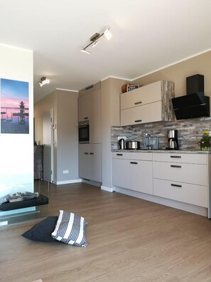 Uma cozinha moderna com armários claros, painel de fundo de pedra e coifa preta.