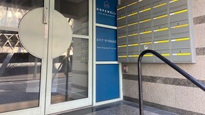 A building entrance with a glass door, a blue sign with contact information, and a row of grey storage lockers with yellow stripes. - Prince Street Studio 2 - Hopewell (Bristol)