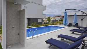 A modern outdoor pool area with a rectangular pool, lounge chairs, and a covered seating area. - Mare Three-bedroom Apartments with Pool and Terrace (Novalja)