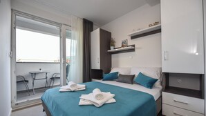 A modern hotel room with a bed, a small table, and a chair by the window. - Mare Three-bedroom Apartments with Pool and Terrace (Novalja)
