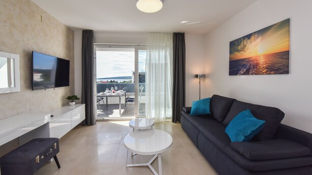 A modern living room with a flat-screen TV, a black sofa with blue cushions, a white coffee table, and a painting of a sunset. - Mare Three-bedroom Apartments with Pool and Terrace (Novalja)