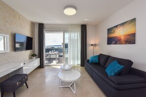 A modern living room with a flat-screen TV, a black sofa with blue cushions, a white coffee table, and a painting of a sunset.