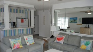 Ein Wohnzimmer mit zwei grauen Sofas, jedes mit einem farbenfrohen Kissen, einem weißen Couchtisch und einer Küchenzeile im Hintergrund.