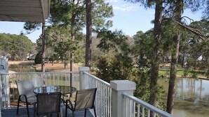 A covered outdoor deck with a table and chairs, overlooking a lake and surrounded by trees.
