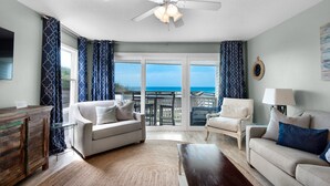 A spacious living room with a large sliding glass door leading to a balcony with a view of the ocean. - Gulf Front, Amazing Views, Beach Setup, Bare Feet Retreat + FreeTickets! (Seacrest)
