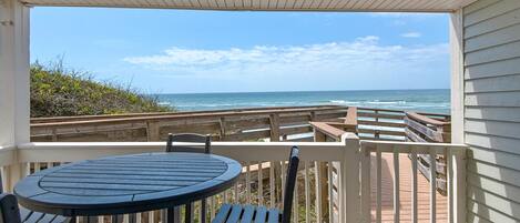 A covered outdoor area with a table and chairs, overlooking the ocean.
