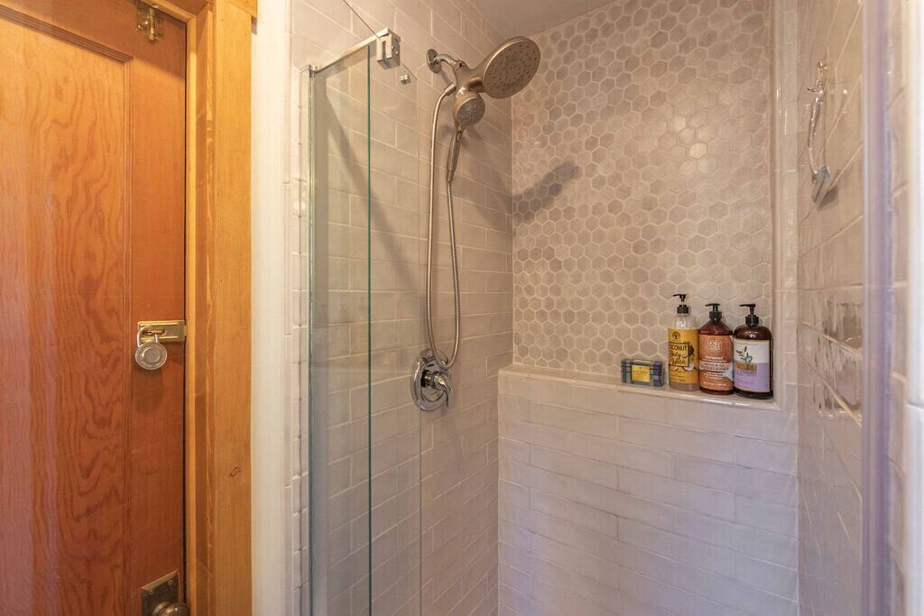 Une douche avec une porte en verre, une porte en bois et un mur carrelé orné de motifs hexagonaux.