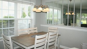 A dining area with a wooden table and white chairs, large windows with blinds, and a mirror on the wall. - 2503m 1 Bedroom Condo by RedAwning (Calabash)