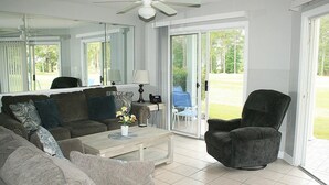 A living room with a sofa, armchair, coffee table, and a view through glass doors to an outdoor area. - 2503m 1 Bedroom Condo by RedAwning (Calabash)