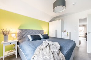 Ein modernes Schlafzimmer mit einem großen Bett, einem Nachttisch mit Lampe, einem Kleiderschrank und Blick ins Freie.