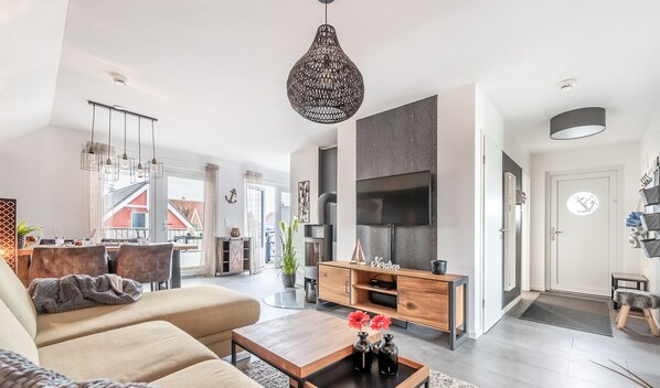 Ein modernes Wohnzimmer mit Sofa, Couchtisch und TV-Schrank. Es gibt eine Essecke mit Stühlen und Tisch, und im Hintergrund eine Küche.