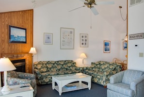 Un salon avec une cheminée, deux canapés à motifs, une table basse et un ventilateur de plafond.