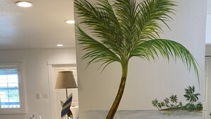 Een kamer met een muurschildering van een palmboom en een strand.