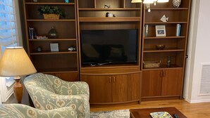 Een woonkamer met een televisie, houten planken, gestreept fauteuils en een salontafel.