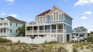 Una propiedad frente a la playa con una construcción de dos pisos, balcón, patio cercado y zona de arena.