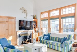 A living room with a fireplace, a television, a striped sofa, and large windows.