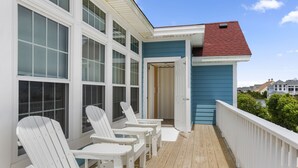 Una terraza de madera con sillas Adirondack blancas, un edificio azul con ventanas grandes y un techo rojo.