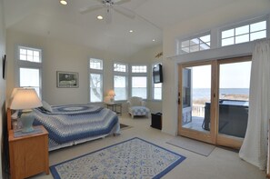 A bedroom with a bed, a chair, a TV, and a view of the sea through a sliding door. - Live Oak Landing: Shared Pool, Spa, Great Views! (Corolla)