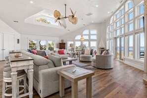 Een ruime woonkamer met een hoge plafond, grote ramen en uitzicht op het omliggende landschap.
