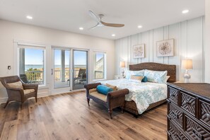 A bedroom with a large bed, two chairs, a dresser, and a ceiling fan. There are two windows with a view of the beach. - Bella Costa: Gourmet Kitchen, Pool, Spa, Elevator (Corolla)