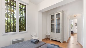 A bedroom with two beds, a white wardrobe, and a window with a view of trees.
