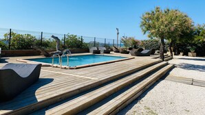 A wooden deck with a pool, lounge chairs, and a tree.