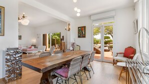 A spacious dining area with a wooden table and wicker chairs, a white sofa, and a red chair.