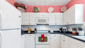 Una cocina con armarios blancos, microondas, estufa y cafetera.