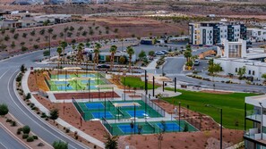 A modern building with multiple floors, a parking lot, and a tennis court area. - Desert Color Lake House: Desert Color Lagoon + Beaches (St. George)