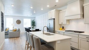 A modern kitchen with a central island, white cabinetry, and a stainless steel refrigerator. - Desert Color Lake House: Desert Color Lagoon + Beaches (St. George)