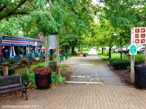 A pathway lined with benches and a trash bin, leading to a restaurant with outdoor seating.