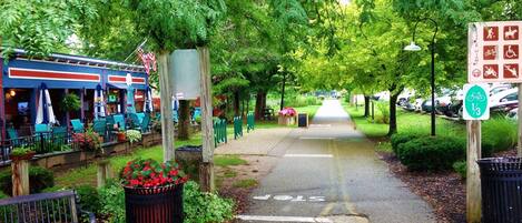 A pathway lined with benches and a trash bin, leading to a restaurant with outdoor seating.